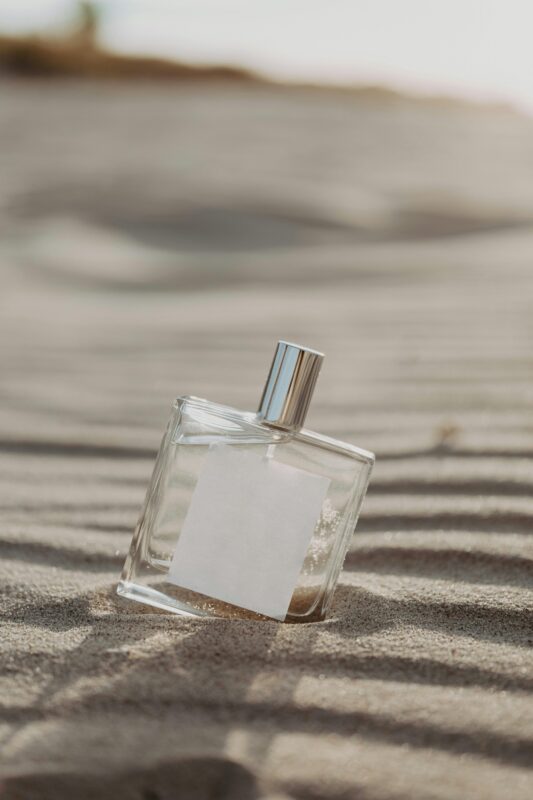 Best Unisex Perfumes 2025: Irresistible Scents in India That Turn Heads Everywhere 8 Minimalist glass perfume bottle on sand, evoking a fresh and beachy fragrance vibe.