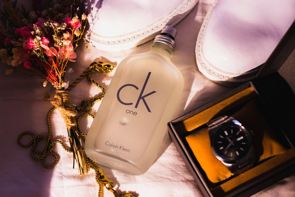 The Return of a Classic: Why Gen Z Is Falling in Love with Calvin Klein One perfume 100Ml Again ? 10 Chic flat lay with CK One bottle, white shoes, watch, flowers and jewelry in warm light.